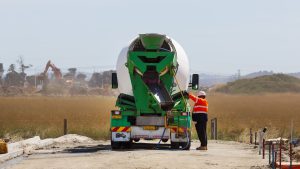 A worker in hi-vis operating the chute of a green concrete mixer truck