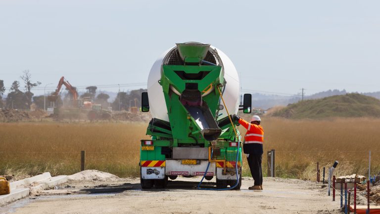 A worker in hi-vis operating the chute of a green concrete mixer truck