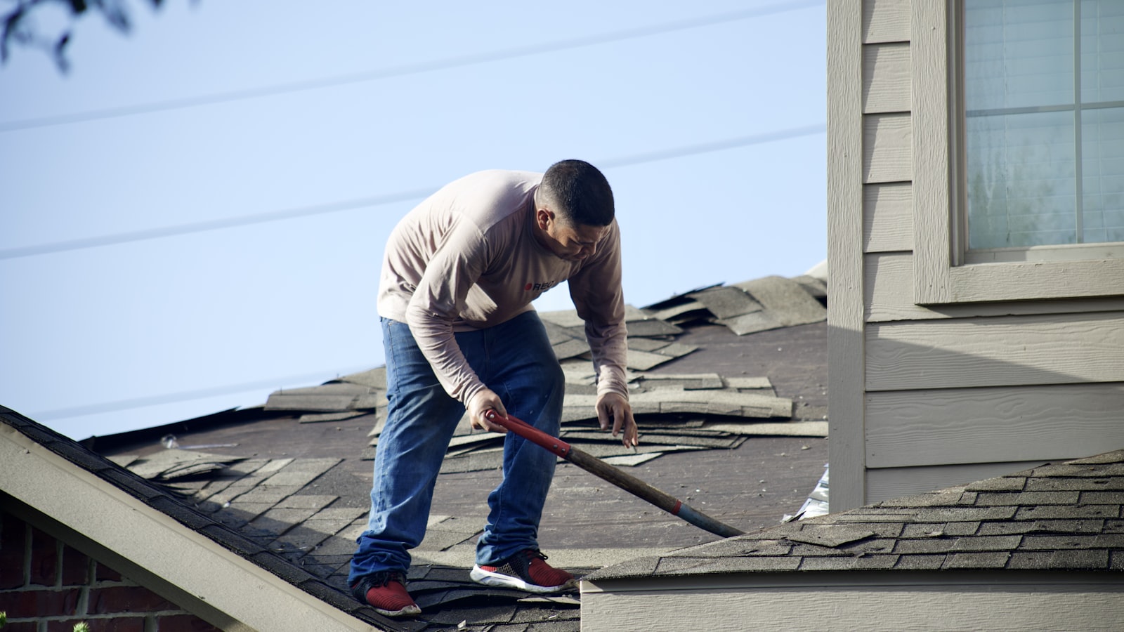 A person in a long-sleeved shirt removing shingles from a residential roof