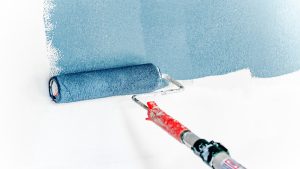 A paint roller applying blue paint to a white wall