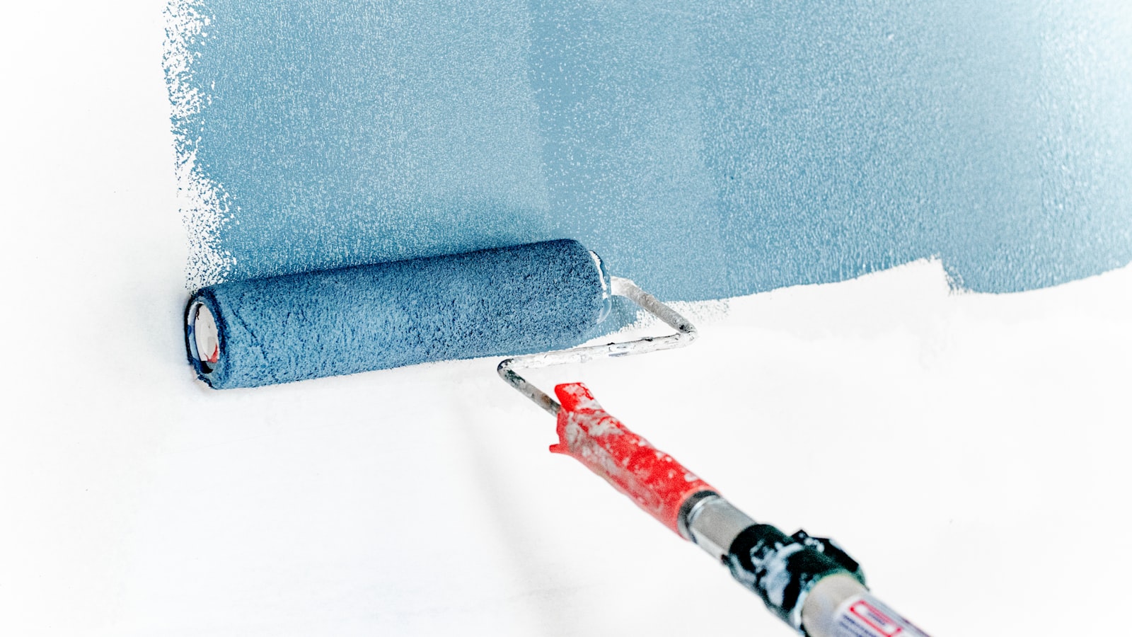 A paint roller applying blue paint to a white wall