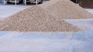 Two large piles of light-colored gravel on concrete pavement
