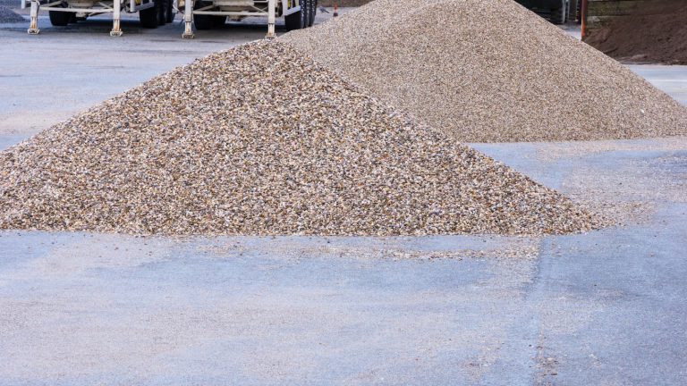 Two large piles of light-colored gravel on concrete pavement
