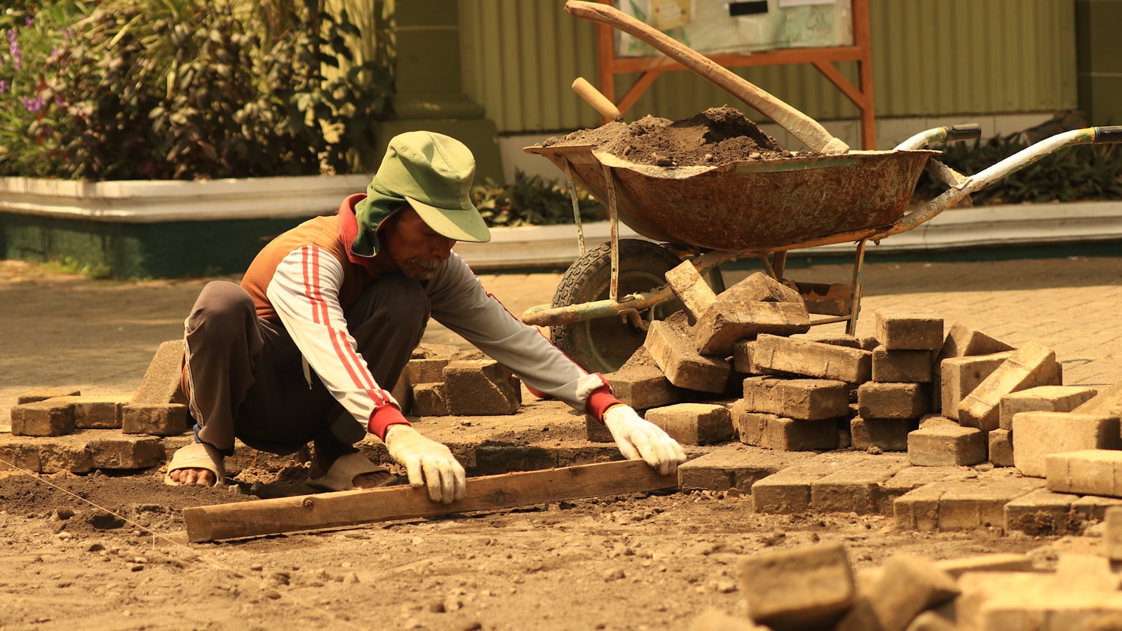 A man laying bricks on the ground in front of a wheelbarrow