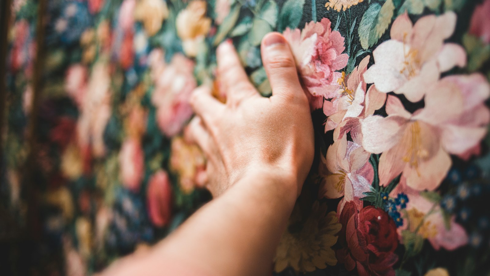 A hand resting on floral patterned wallpaper