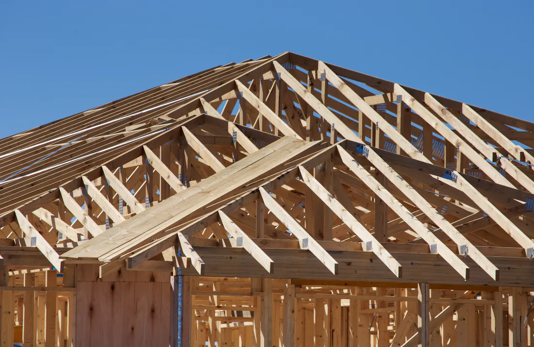Wooden roof trusses on a house under construction against a clear blue sky